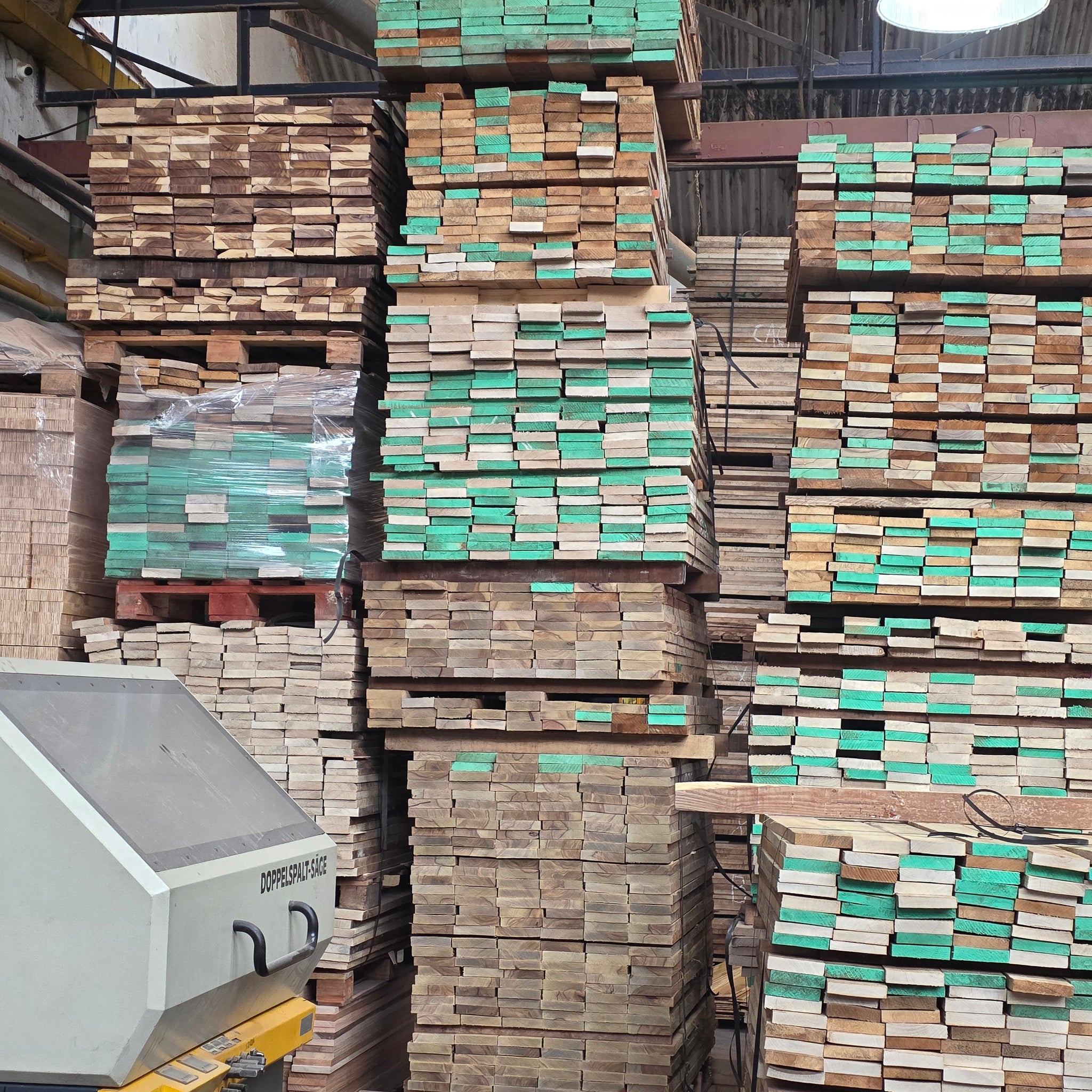 Stacks of wooden planks in a warehouse setting with a machine on the left.